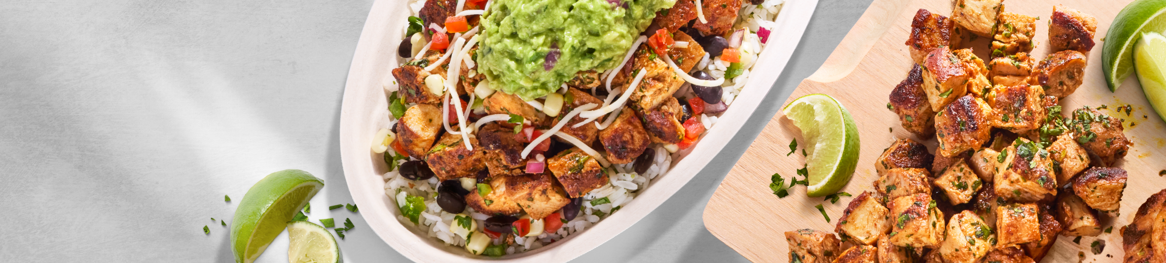 A Chipotle Pollo Asado bowl resting on a table next to a cutting board with freshly made Pollo Asado and a slice of lime.